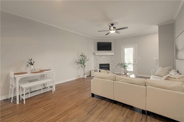 living room featuring hardwood / wood-style floors, ceiling fan, a stone fireplace, and ornamental molding