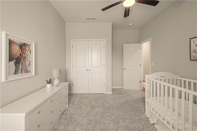 carpeted bedroom with ceiling fan, a nursery area, and a closet