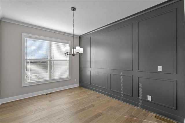 unfurnished dining area with crown molding, a notable chandelier, and light wood-type flooring