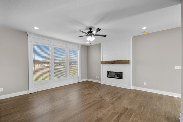 unfurnished living room with ceiling fan, a large fireplace, and dark hardwood / wood-style floors