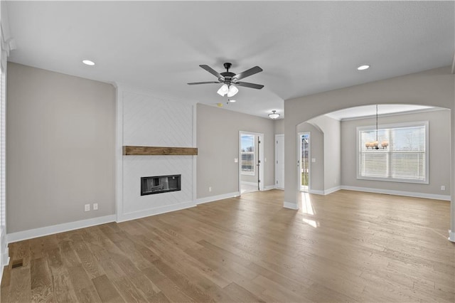 unfurnished living room with a fireplace, ceiling fan with notable chandelier, and light wood-type flooring