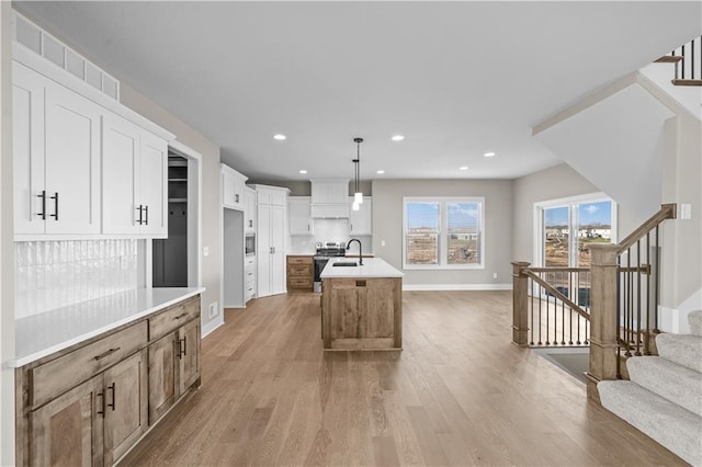 kitchen featuring pendant lighting, white cabinets, electric stove, light wood-type flooring, and an island with sink