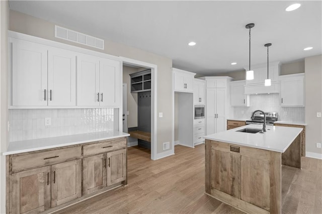 kitchen with tasteful backsplash, light hardwood / wood-style floors, decorative light fixtures, a kitchen island with sink, and white cabinets