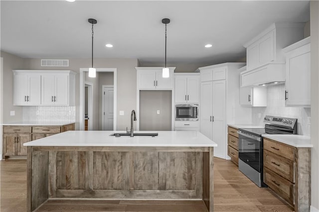 kitchen featuring white cabinetry, hardwood / wood-style floors, pendant lighting, a center island with sink, and appliances with stainless steel finishes