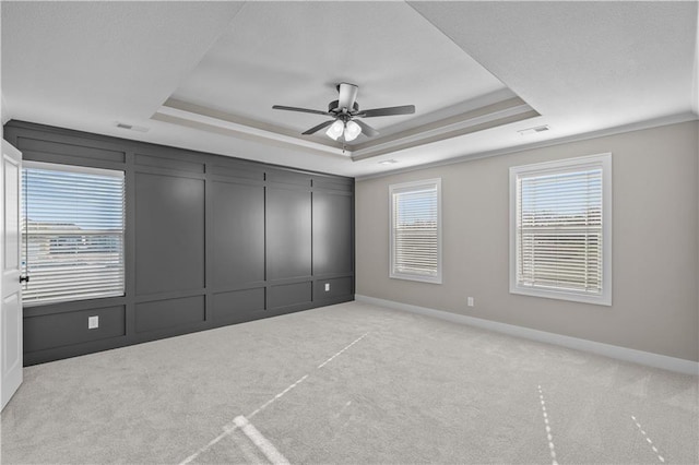 unfurnished bedroom with ceiling fan, a raised ceiling, light carpet, and crown molding