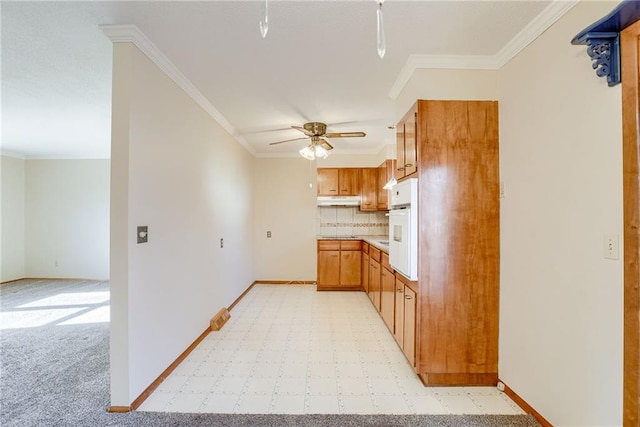 5032 NE 57th Ter, Kansas City, MO 64119 - kitchen featuring under cabinet range hood, a ceiling fan, ornamental molding, decorative backsplash, and light colored carpet