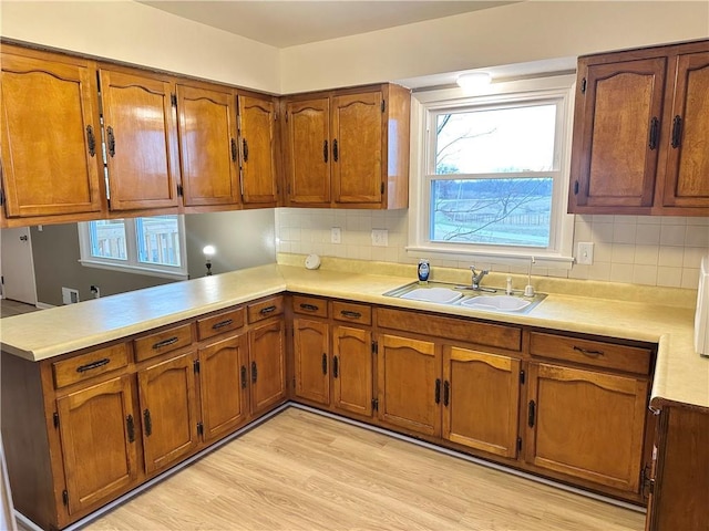 kitchen featuring backsplash, kitchen peninsula, sink, and light hardwood / wood-style flooring