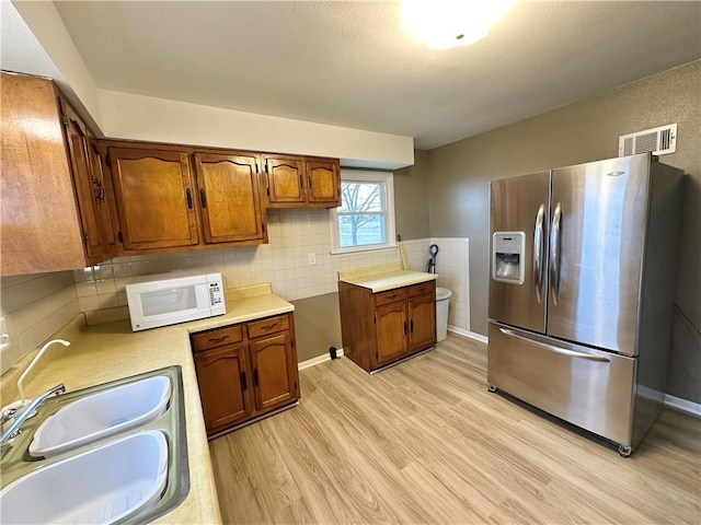 kitchen with stainless steel fridge, light wood-type flooring, tile walls, and sink