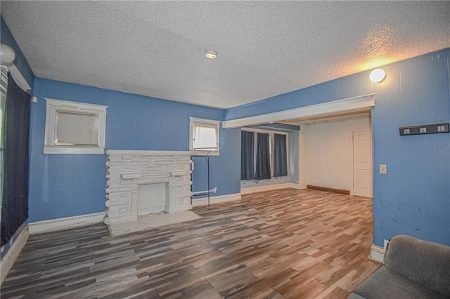 unfurnished living room with hardwood / wood-style flooring, a stone fireplace, and a textured ceiling