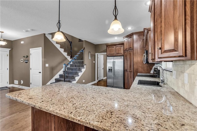 kitchen with light stone countertops, sink, stainless steel appliances, backsplash, and pendant lighting