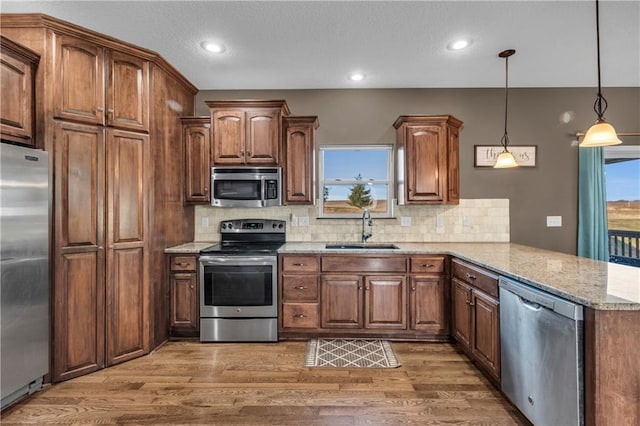 kitchen with sink, hanging light fixtures, tasteful backsplash, kitchen peninsula, and appliances with stainless steel finishes