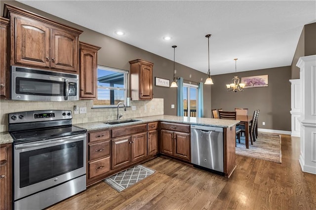 kitchen featuring kitchen peninsula, appliances with stainless steel finishes, tasteful backsplash, sink, and hanging light fixtures