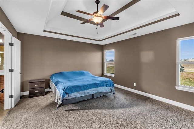 bedroom featuring carpet flooring, multiple windows, a tray ceiling, and ceiling fan