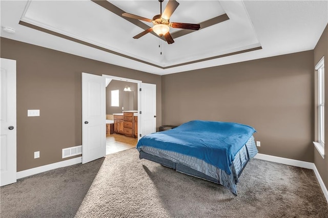 carpeted bedroom with ensuite bathroom, ceiling fan, and a raised ceiling