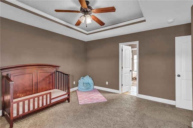 bedroom with a raised ceiling, ceiling fan, ornamental molding, a nursery area, and light colored carpet