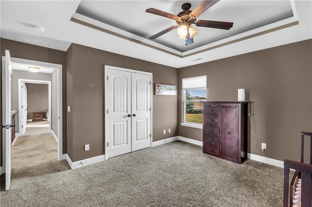 unfurnished bedroom with a raised ceiling, ceiling fan, a closet, and carpet