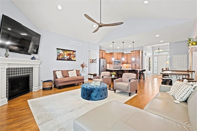 living room featuring a tile fireplace, recessed lighting, ceiling fan with notable chandelier, visible vents, and light wood-style floors