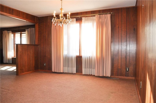 carpeted spare room featuring wooden walls, plenty of natural light, and a notable chandelier