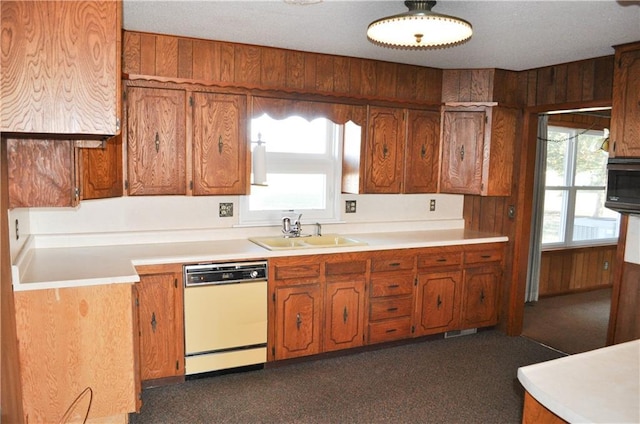 kitchen featuring white dishwasher, wooden walls, and sink