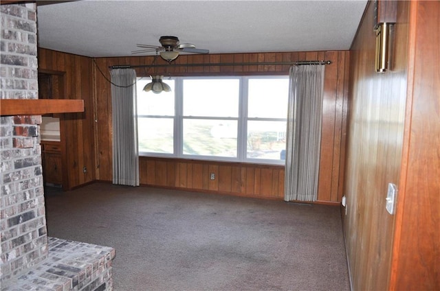 unfurnished living room with carpet flooring, wood walls, ceiling fan, and a textured ceiling