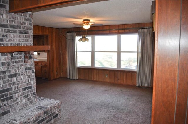 unfurnished living room featuring wooden walls, carpet, a textured ceiling, and ceiling fan