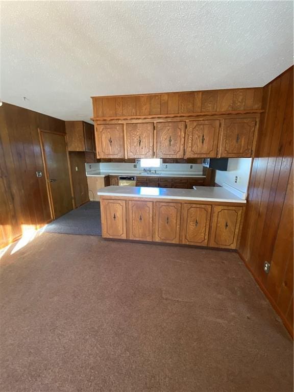 kitchen featuring dark colored carpet, dishwashing machine, a textured ceiling, and wooden walls