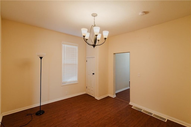 spare room featuring dark hardwood / wood-style flooring and an inviting chandelier