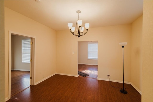 unfurnished room featuring plenty of natural light, dark wood-type flooring, and a chandelier