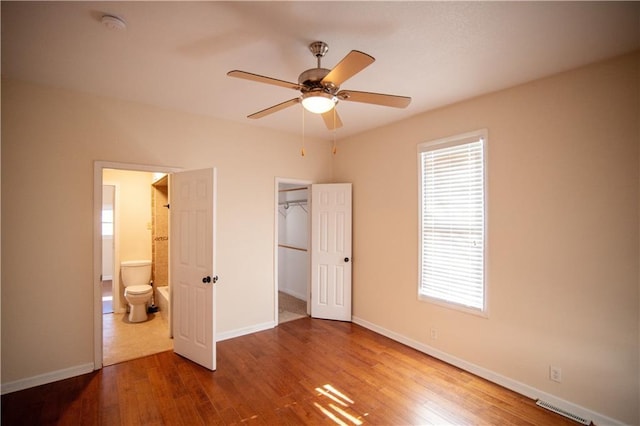 unfurnished bedroom featuring ensuite bath, a spacious closet, ceiling fan, a closet, and hardwood / wood-style flooring