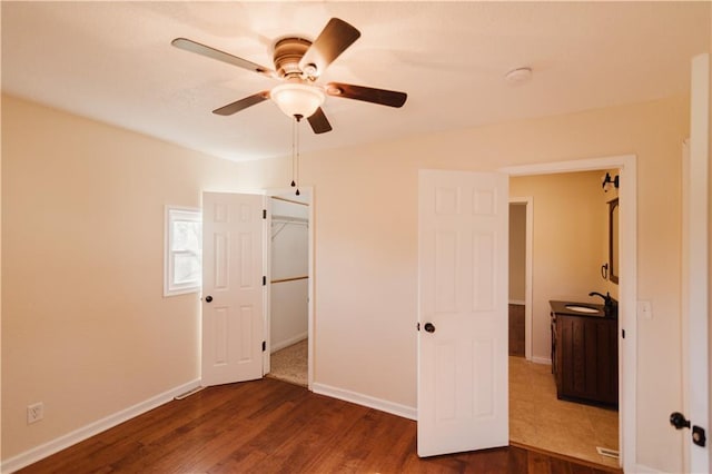 unfurnished bedroom featuring ceiling fan, a spacious closet, sink, dark wood-type flooring, and a closet