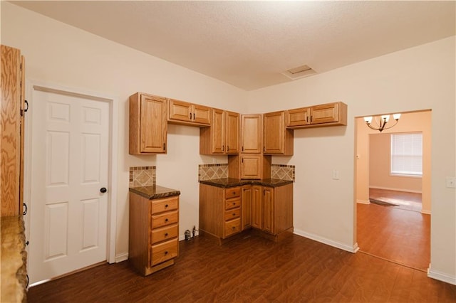 kitchen featuring decorative backsplash, dark stone counters, dark wood-type flooring, and a notable chandelier