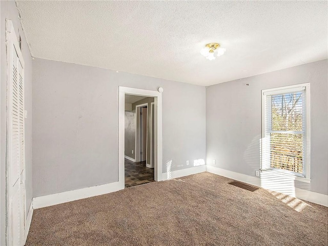 carpeted empty room featuring a textured ceiling, visible vents, and baseboards