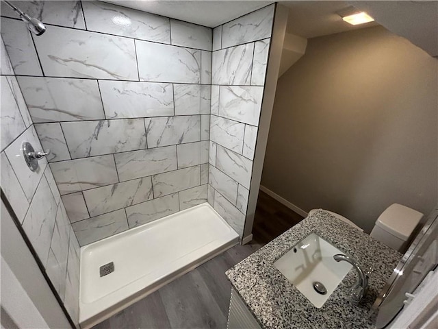 bathroom with tiled shower, vanity, hardwood / wood-style flooring, and toilet