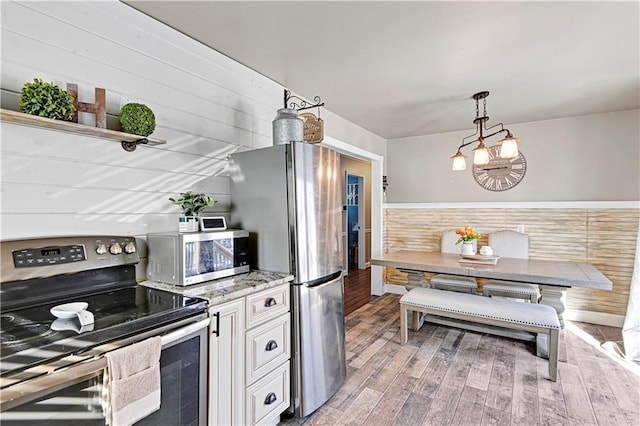 kitchen featuring pendant lighting, white cabinetry, light stone counters, wood-type flooring, and stainless steel appliances