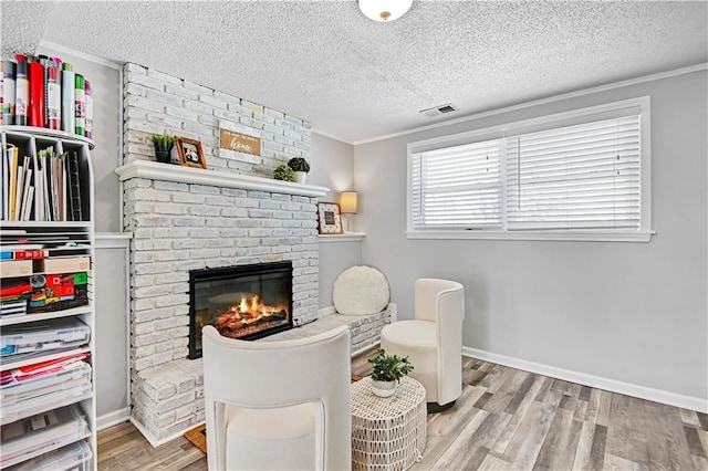 living area with crown molding, light hardwood / wood-style floors, a textured ceiling, and a brick fireplace