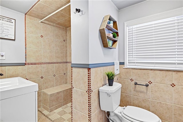 bathroom with crown molding, toilet, tiled shower, vanity, and tile walls