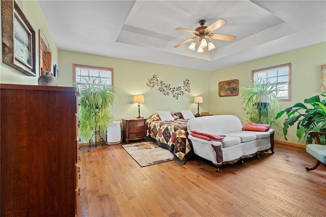 bedroom with light hardwood / wood-style floors, a raised ceiling, and multiple windows