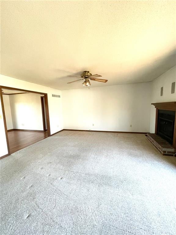 unfurnished living room featuring ceiling fan, a fireplace, carpet floors, and a textured ceiling