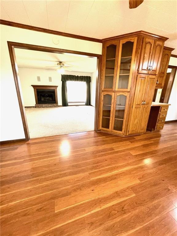 unfurnished living room featuring hardwood / wood-style floors, ceiling fan, built in desk, and crown molding