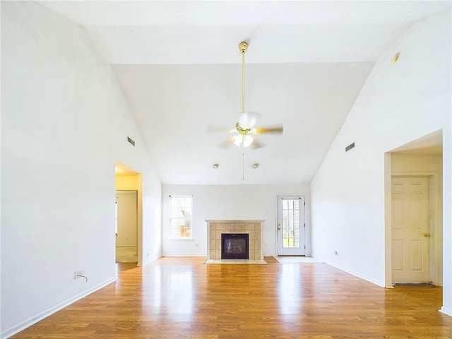 unfurnished living room featuring a tile fireplace, high vaulted ceiling, ceiling fan, and light wood-type flooring