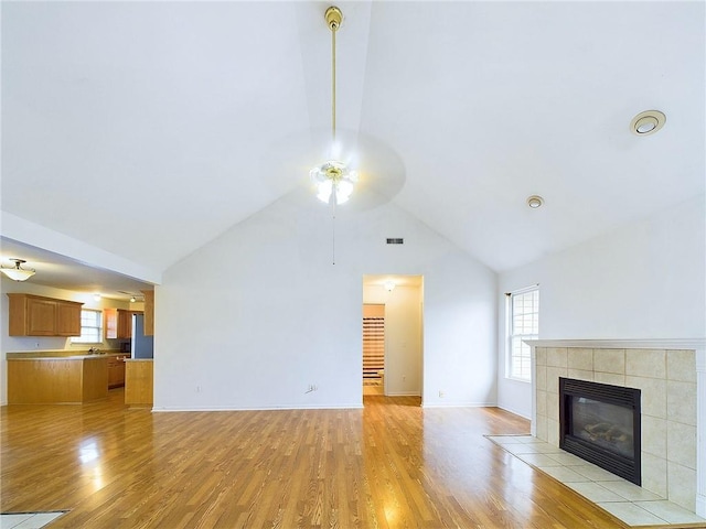 unfurnished living room with a tiled fireplace, high vaulted ceiling, and light wood-type flooring