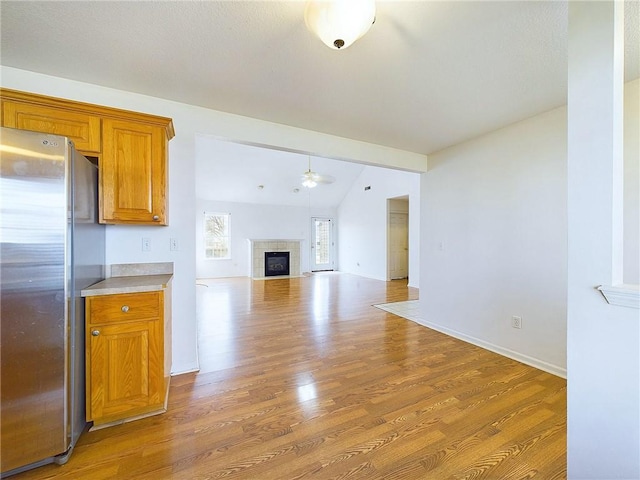 unfurnished living room featuring ceiling fan, hardwood / wood-style floors, vaulted ceiling, and a tile fireplace