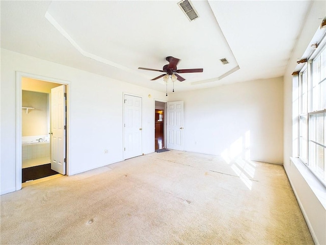 unfurnished bedroom with connected bathroom, a raised ceiling, and light carpet