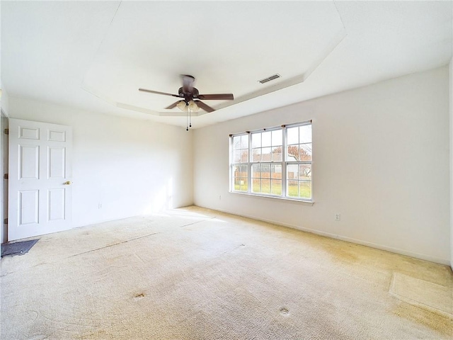 spare room with a raised ceiling, light carpet, and ceiling fan