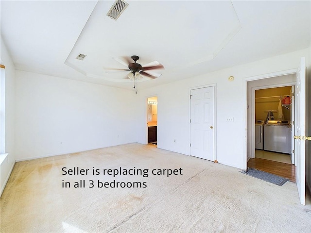 unfurnished bedroom featuring washer and clothes dryer, ceiling fan, connected bathroom, a tray ceiling, and carpet floors