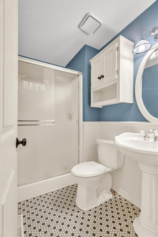 bathroom with tile patterned flooring, a textured ceiling, toilet, and an enclosed shower