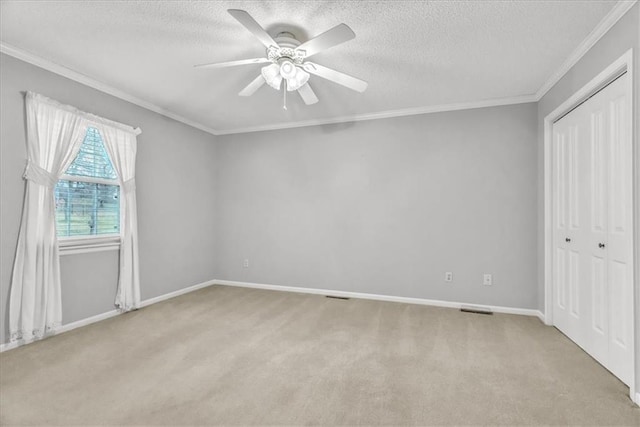 unfurnished bedroom featuring ceiling fan, crown molding, a textured ceiling, light carpet, and a closet