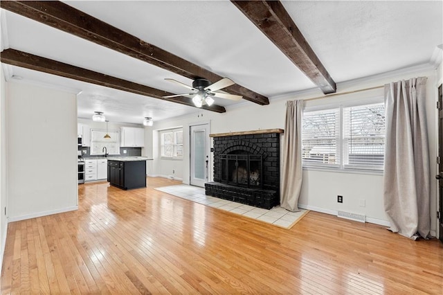 unfurnished living room with light wood-type flooring, ceiling fan, sink, beam ceiling, and a fireplace