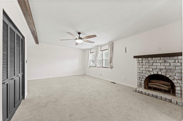 unfurnished living room with carpet flooring, ceiling fan, beamed ceiling, and a brick fireplace