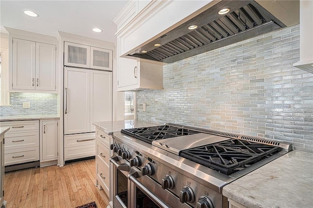 kitchen featuring light hardwood / wood-style floors, custom range hood, tasteful backsplash, stainless steel range, and white cabinets